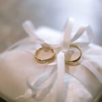Close-up of two gold wedding rings on a satin pillow tied with ribbons, symbolizing marriage.