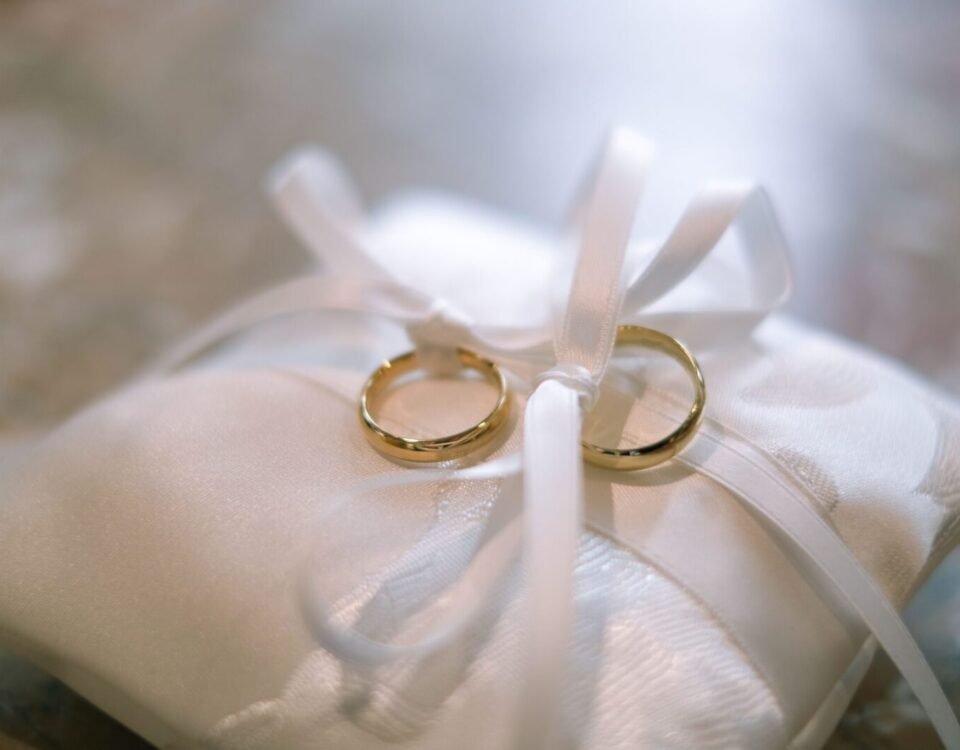 Close-up of two gold wedding rings on a satin pillow tied with ribbons, symbolizing marriage.