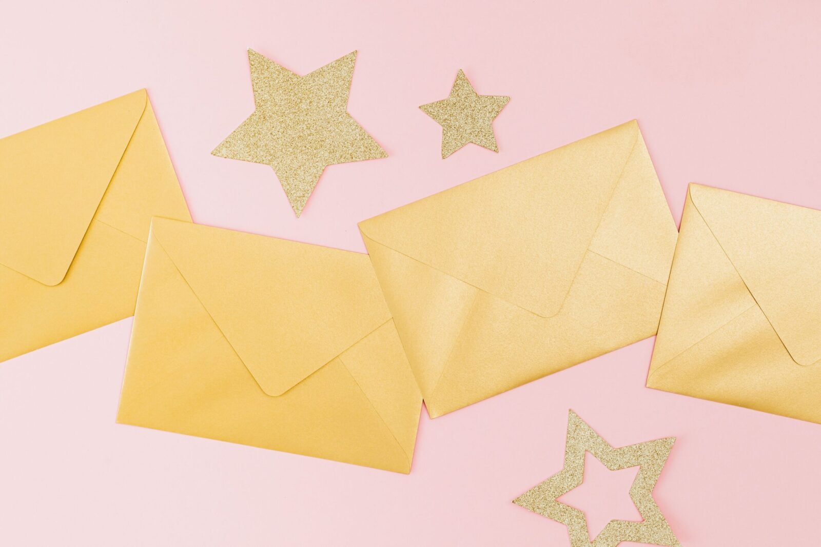 Golden envelopes and glittery stars on a pink background, perfect for festive celebrations.